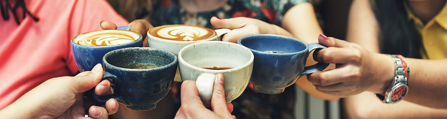 Women holding cups of coffee together to cheers
